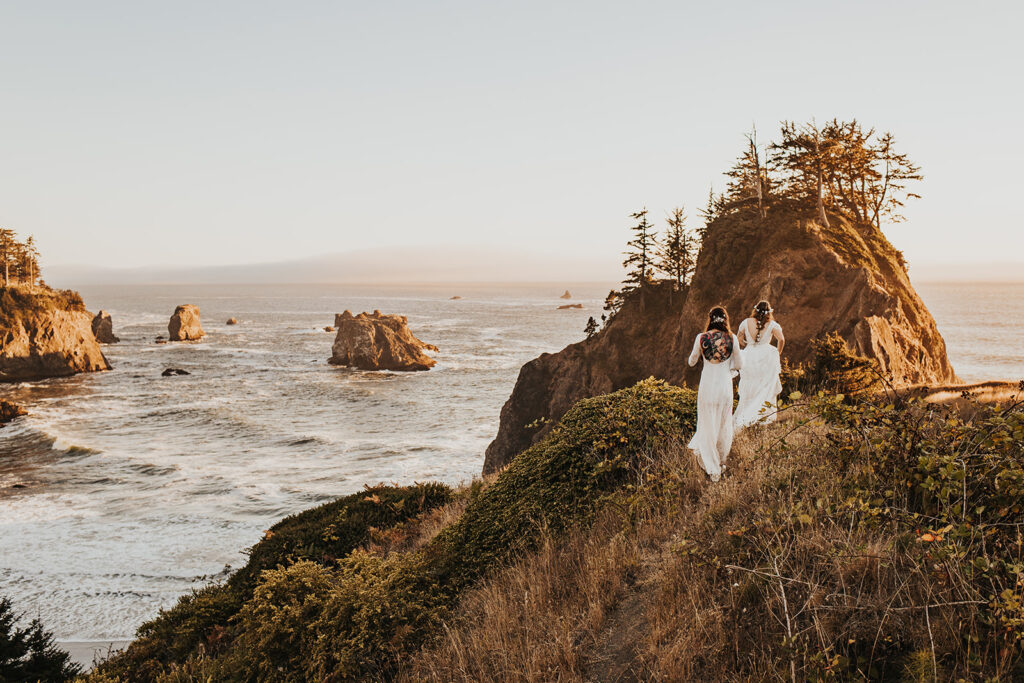 Two brides walk along an ocean bluff on the Oregon Coast at sunset