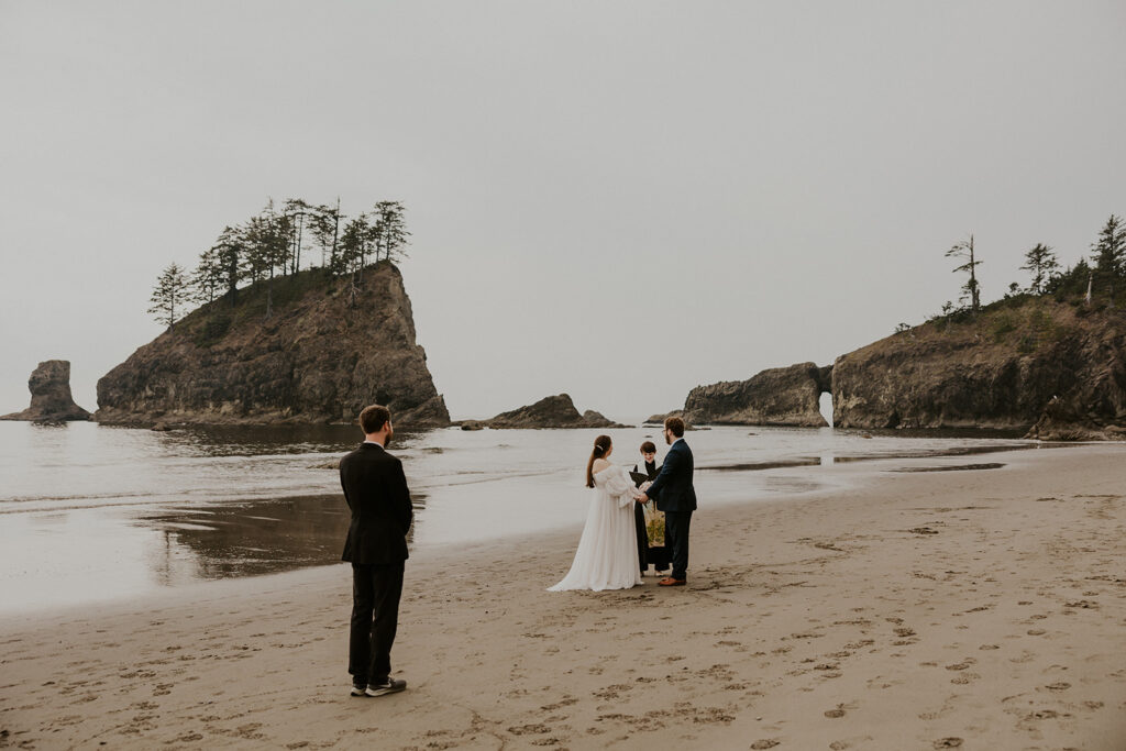 A wedding couple, an officiant, and one guest stand on a beach on the Oregon Coast for an elopement ceremony