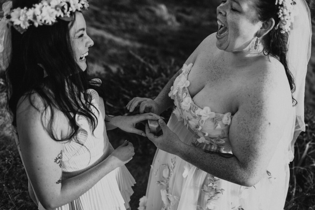 Two brides are laughing and exchanging rings during a wedding ceremony on the Oregon Coast