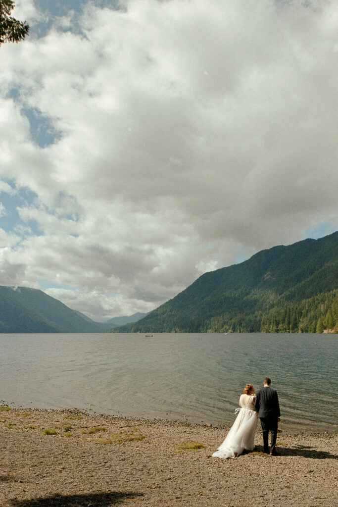 A couple in wedding attire walk along the edge of Lake Crescent in Olympic National Park on 35mm film