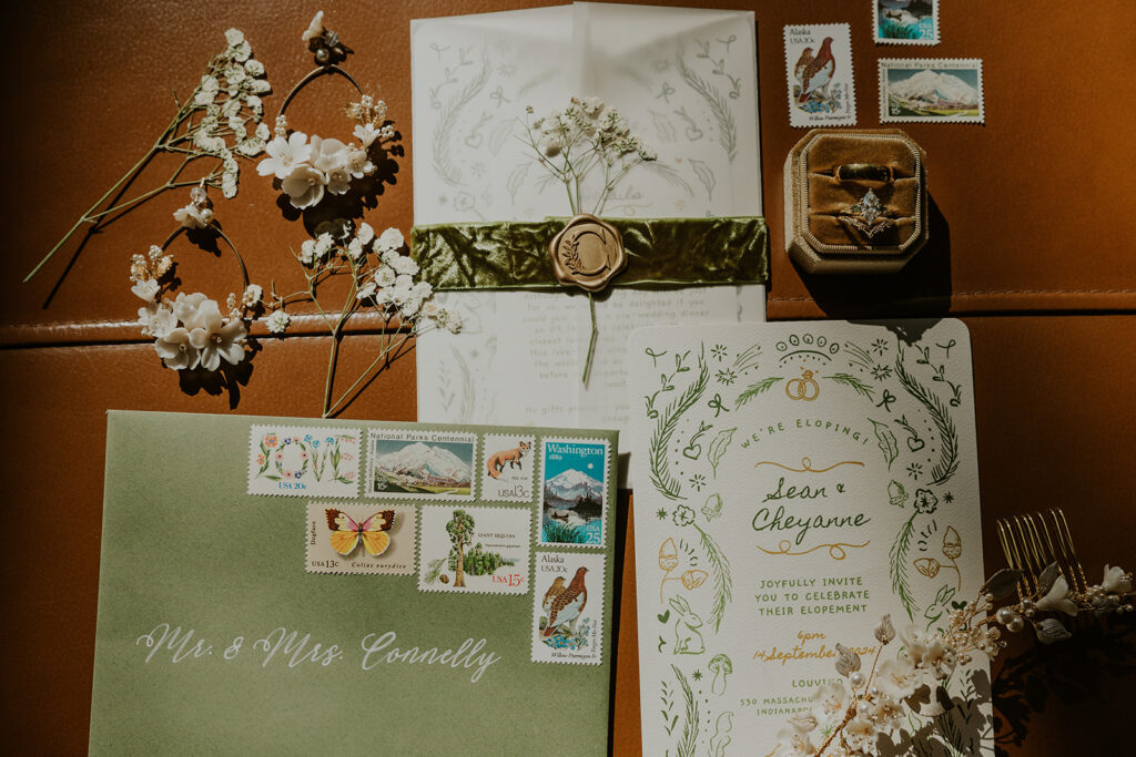 An elopement detail photo featuring an invitation suite, ring box, stamps, and dried florals