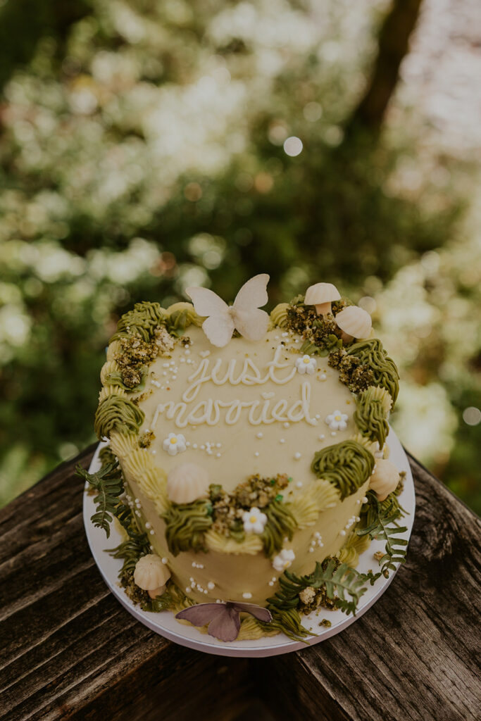 A wedding cake that says "just married" decorated with mushrooms, moss, and butterflies