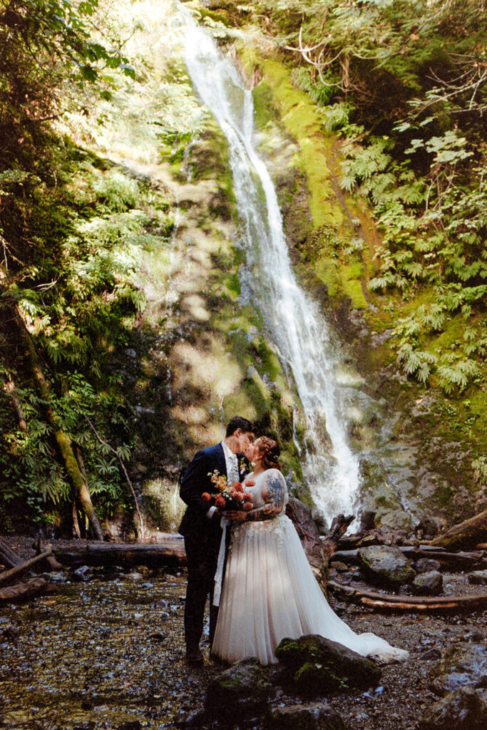 A couple in wedding attire pose by a waterfall in Olympic National Park on 35mm film