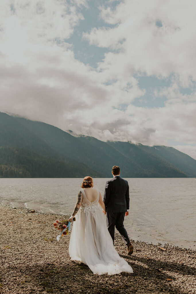 A couple in wedding attire walk along the edge of Lake Crescent in Olympic National Park