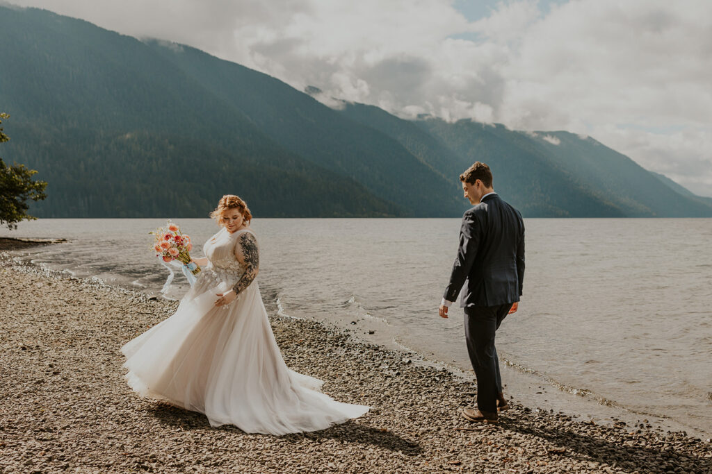 A couple in wedding attire walk along the edge of Lake Crescent in Olympic National Park