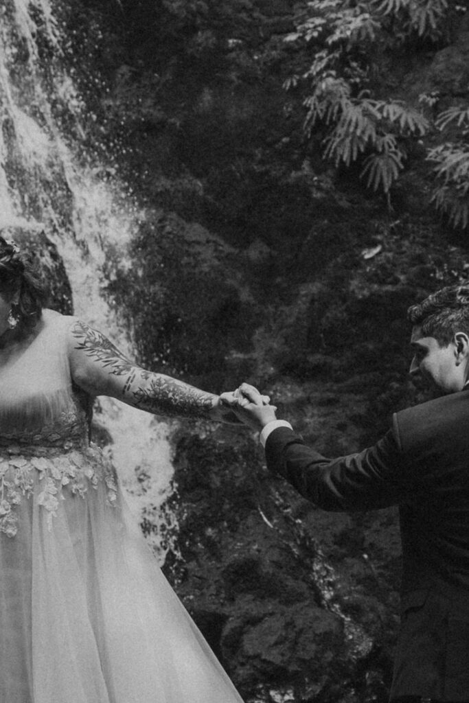 A couple in wedding attire pose by a waterfall in Olympic National Park