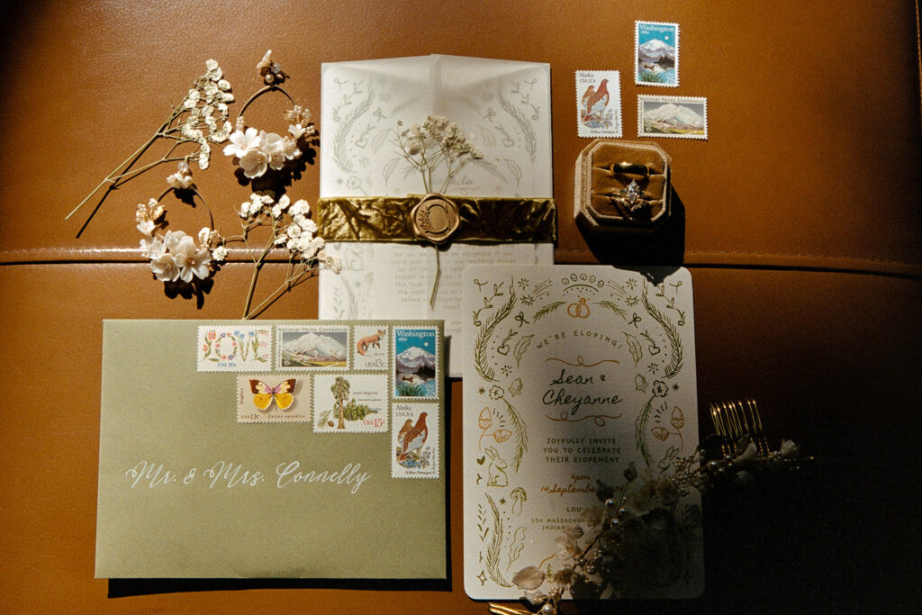 An elopement detail photo featuring an invitation suite, ring box, stamps, and dried florals on 35mm film