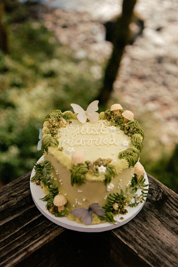 A wedding cake that says "just married" decorated with mushrooms, moss, and butterflies in 35mm film