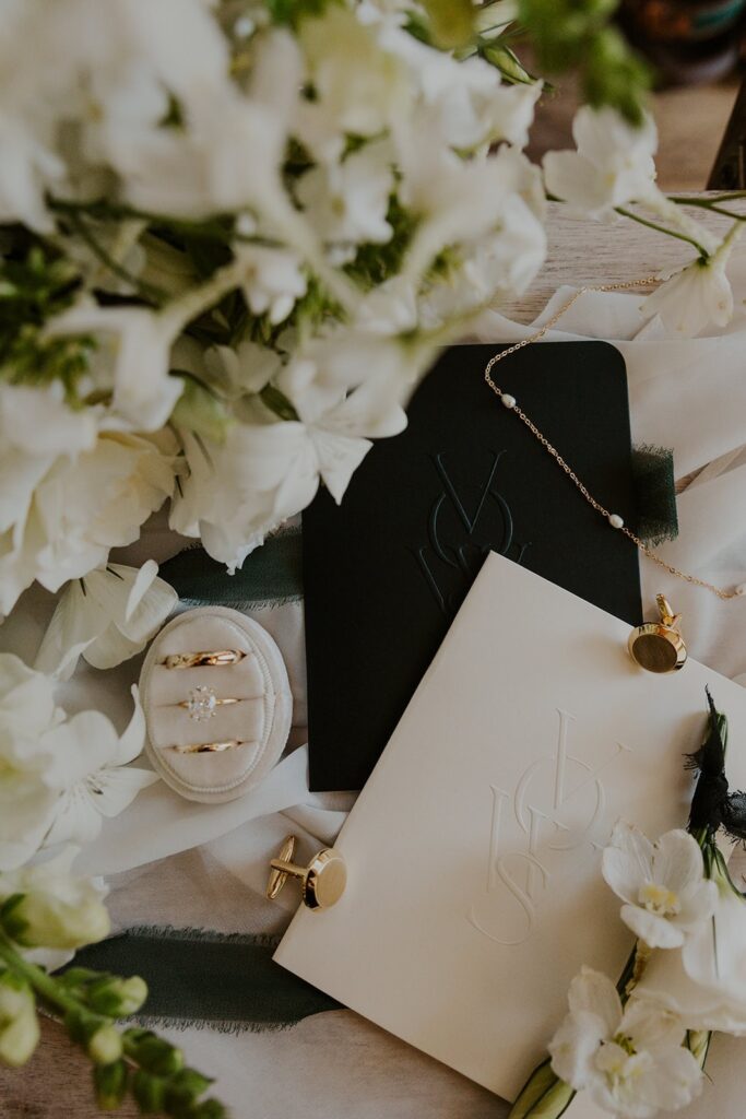 Flay lay for micro wedding featuring rings, vow books, jewelry, and bouquet
