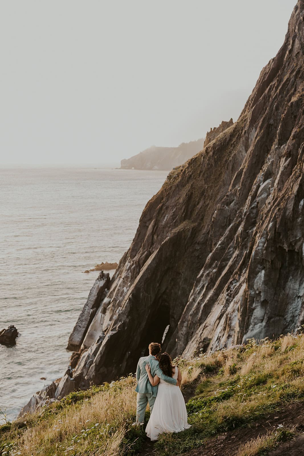 A couple standing on a cliff edge on the Oregon Coast during their elopement day