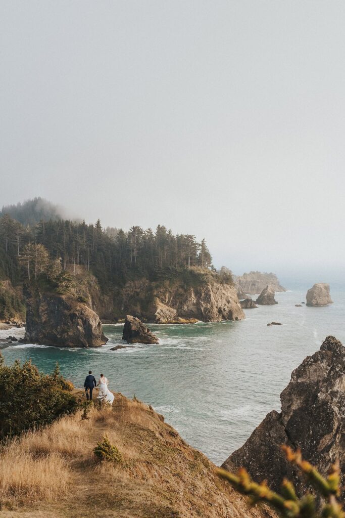 A couple walks along a cliff edge on the Oregon Coast during their elopement wedding