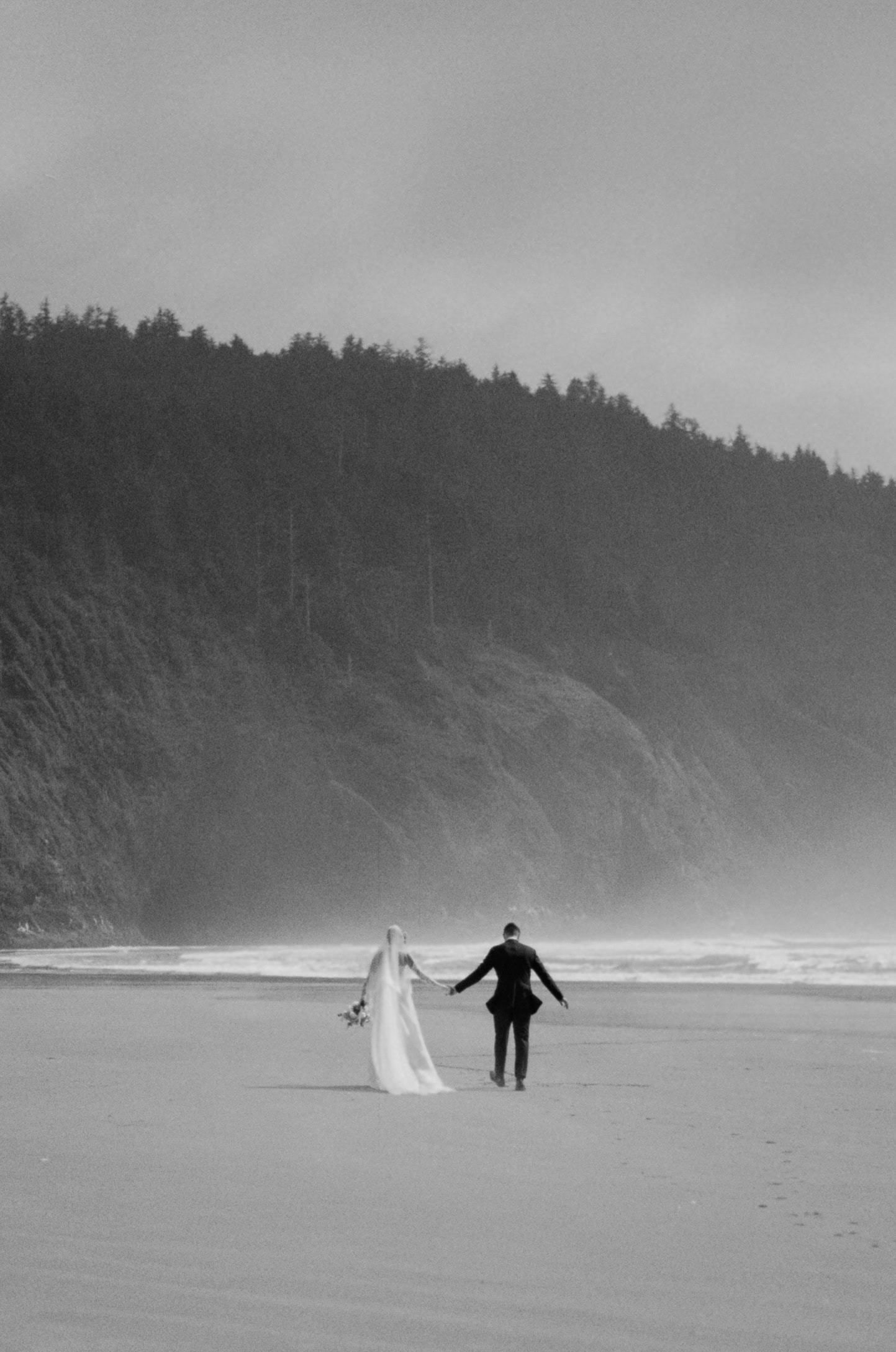 A couple walking on the beach during their elopement day, captured on film in black and white