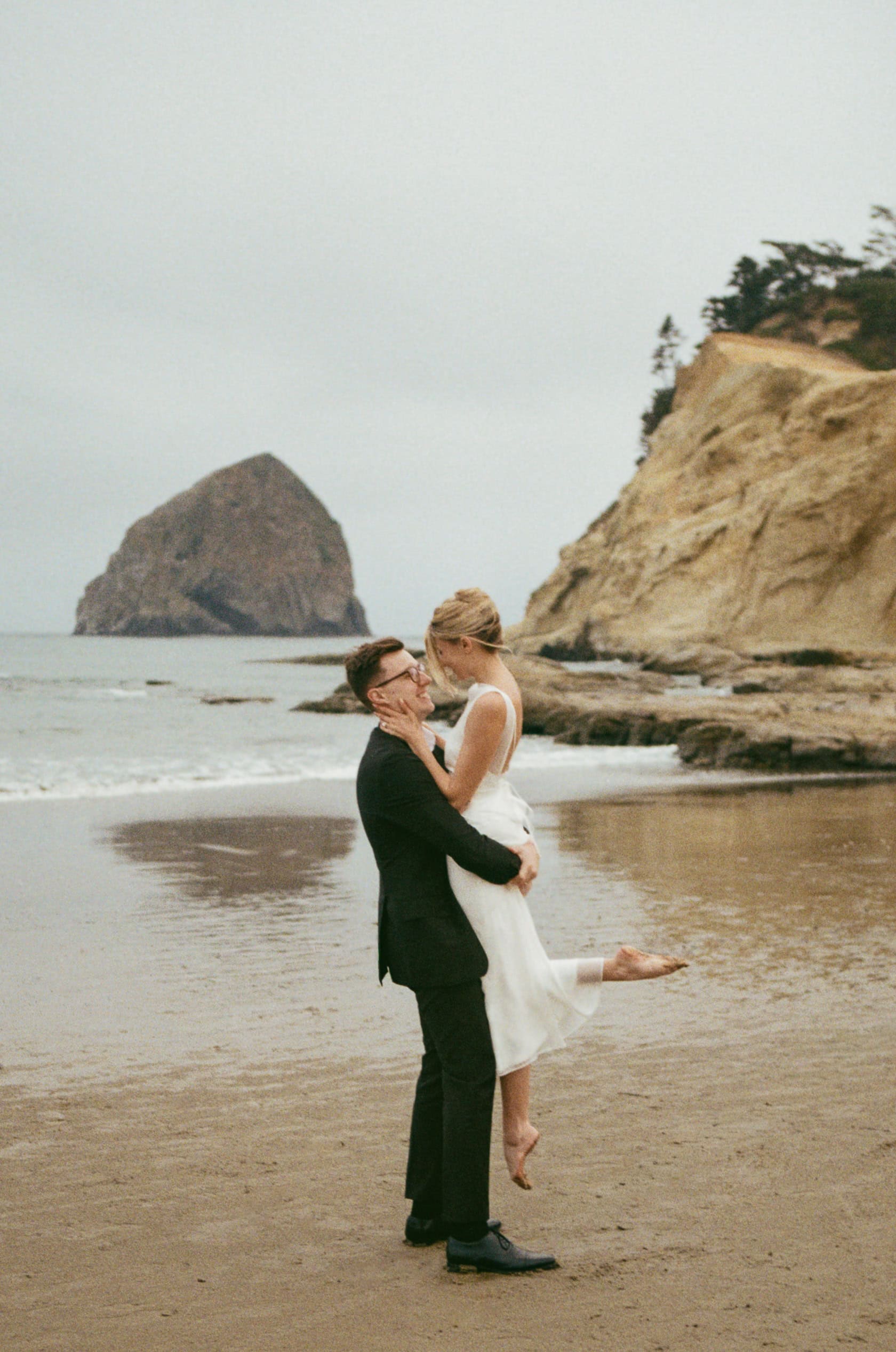 A couple on Cape Kiwanda beach together during their Oregon Coast elopement on 35mm film